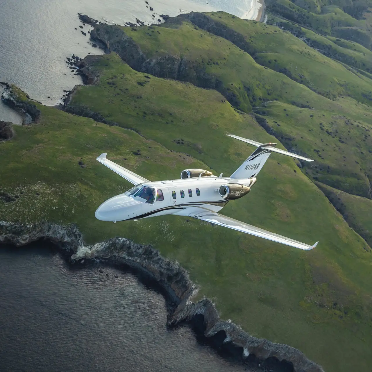 Small airplane flying over green coastal landscape